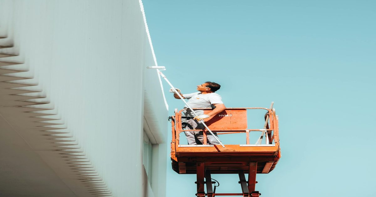 Trabalhador em plataforma elevada pintando fachada de edifício - Trabalho em Altura NR-35 - Simplifica Ocupacional